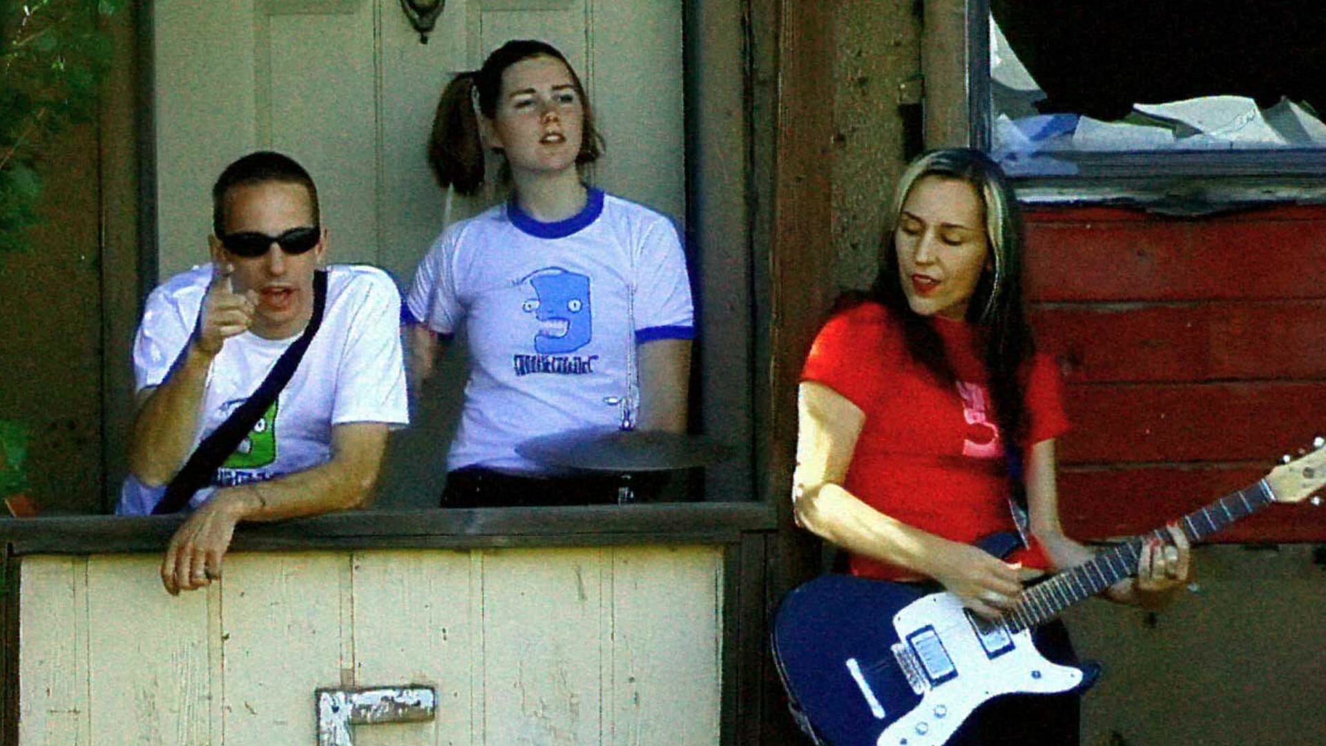 Group of people sitting on a porch playing guitar.